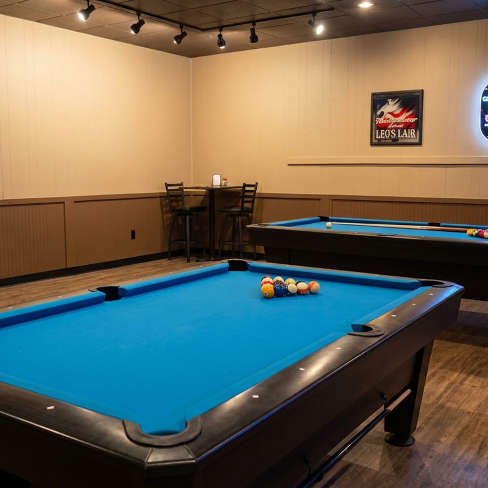 Two blue-felt pool tables with racked billiard balls in a warmly lit restaurant game room.